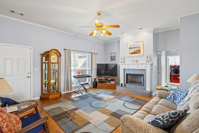 living area featuring a fireplace, wood finished floors, visible vents, ornamental molding, and washer / dryer