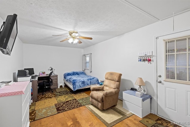 bedroom featuring a textured ceiling, ceiling fan, attic access, and light wood-style floors