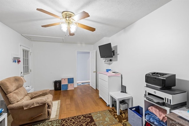 sitting room featuring a textured ceiling, ceiling fan, wood finished floors, and attic access