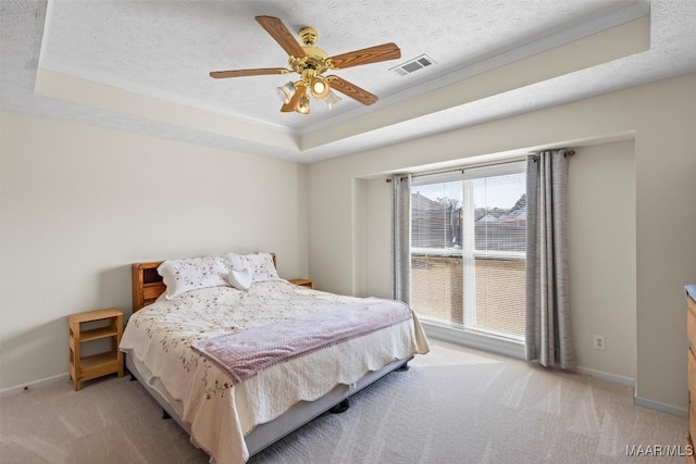 bedroom with a textured ceiling, a tray ceiling, visible vents, and light colored carpet