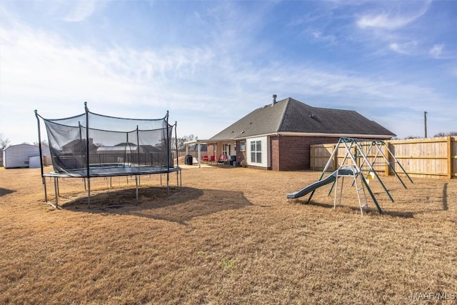 view of yard featuring a trampoline, a playground, and fence