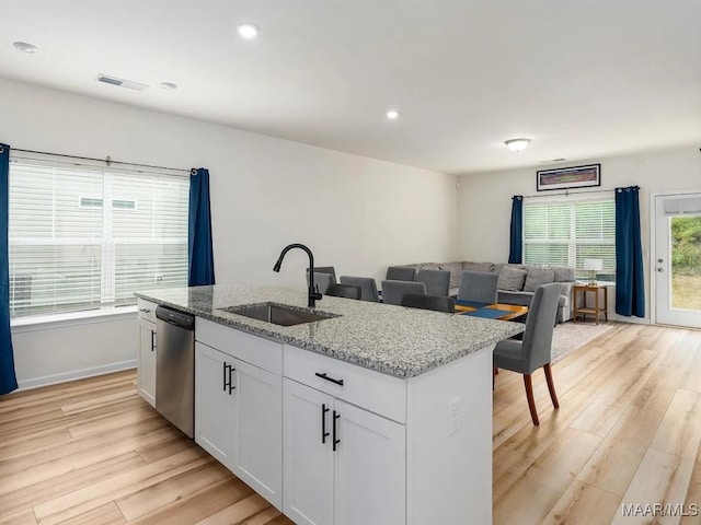 kitchen featuring an island with sink, dishwasher, light wood finished floors, and a sink