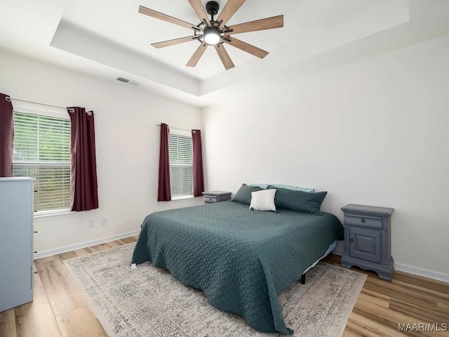 bedroom with visible vents, a raised ceiling, and wood finished floors