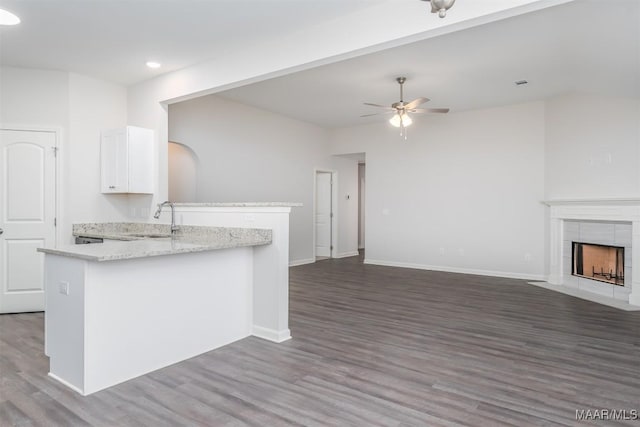 kitchen with a tiled fireplace, a ceiling fan, open floor plan, a peninsula, and a sink