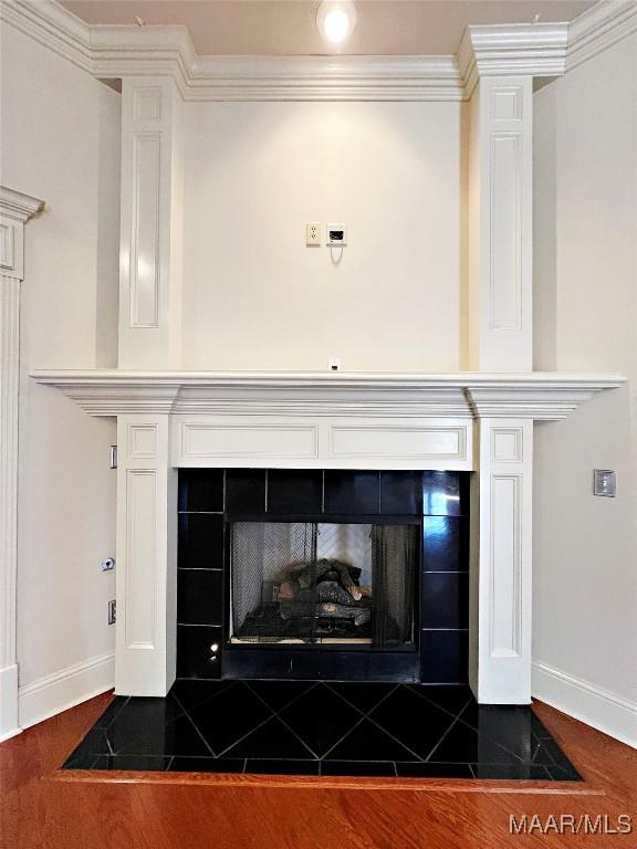 interior details featuring a tiled fireplace, baseboards, crown molding, and wood finished floors