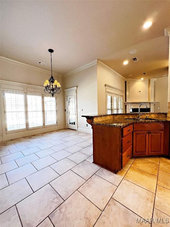 kitchen featuring visible vents, brown cabinets, a peninsula, an inviting chandelier, and a sink