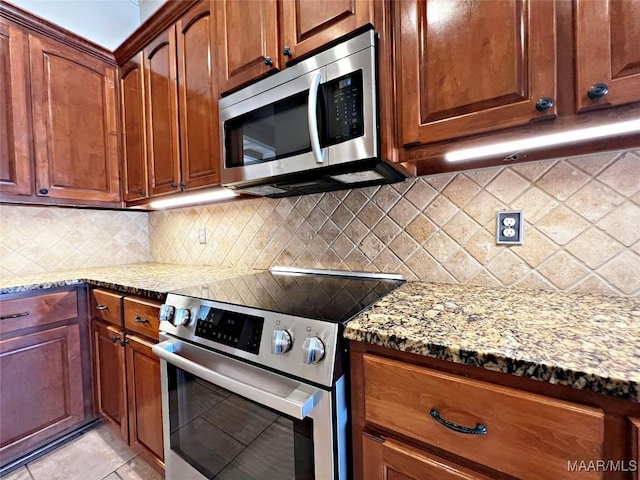 kitchen featuring stainless steel appliances, light stone counters, brown cabinetry, and backsplash