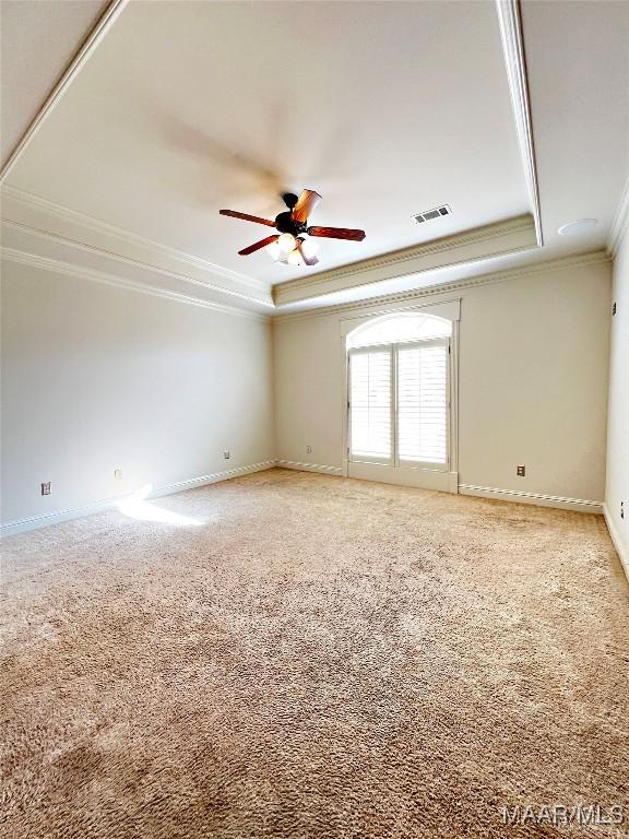 unfurnished room with crown molding, a raised ceiling, light colored carpet, visible vents, and a ceiling fan