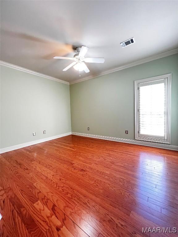 empty room with ceiling fan, visible vents, wood finished floors, and ornamental molding