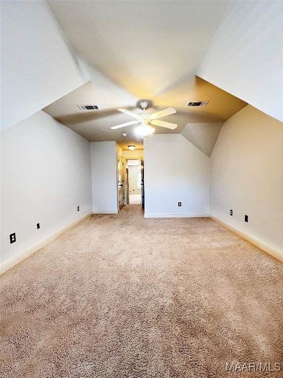 additional living space featuring a ceiling fan, visible vents, vaulted ceiling, and light carpet