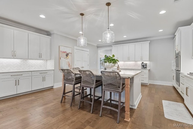 kitchen with hardwood / wood-style flooring, a breakfast bar area, a kitchen island with sink, crown molding, and white cabinetry