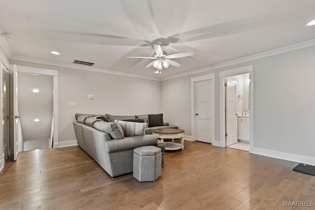 living room featuring wood finished floors, a ceiling fan, visible vents, baseboards, and ornamental molding