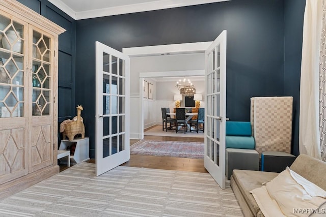 sitting room featuring an inviting chandelier, wood finished floors, crown molding, and french doors