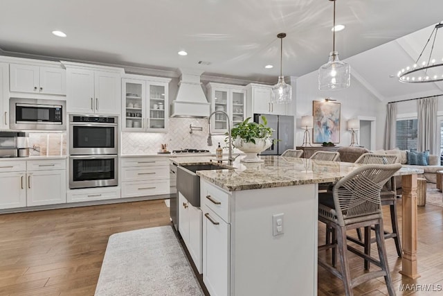 kitchen with stainless steel appliances, premium range hood, vaulted ceiling, open floor plan, and backsplash