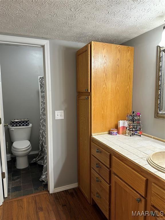 full bathroom with a textured ceiling, vanity, toilet, wood finished floors, and baseboards