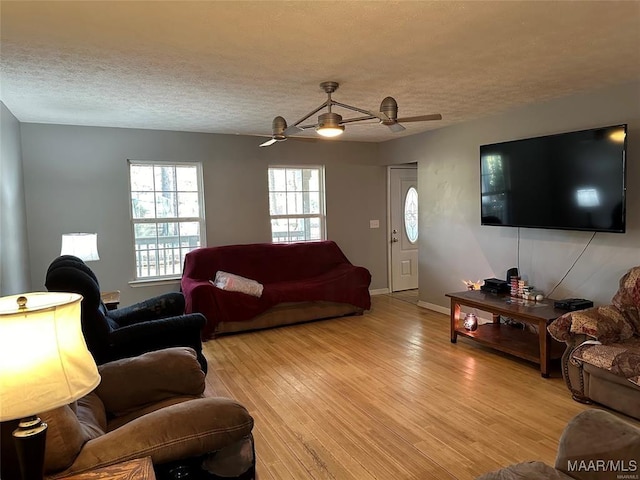 living area featuring ceiling fan, light wood-type flooring, baseboards, and a textured ceiling