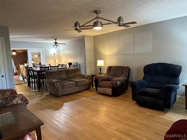 living room with light wood-type flooring, a ceiling fan, and a textured ceiling