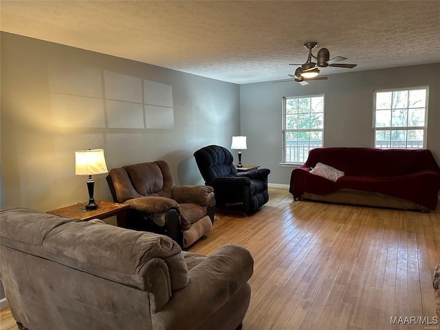 living room with a textured ceiling, wood-type flooring, a ceiling fan, and baseboards