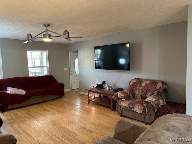 living room featuring a textured ceiling, light wood finished floors, ceiling fan, and baseboards
