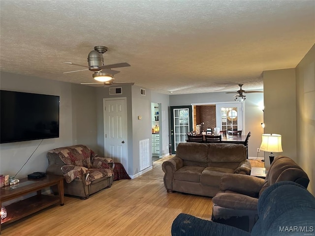 living room featuring a textured ceiling, light wood finished floors, a ceiling fan, and visible vents