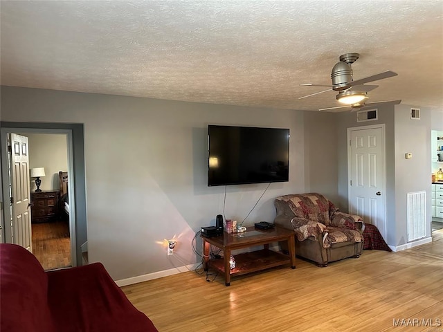 living room featuring wood finished floors, ceiling fan, baseboards, and visible vents