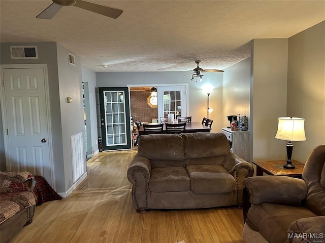 living area with visible vents, a ceiling fan, and wood finished floors