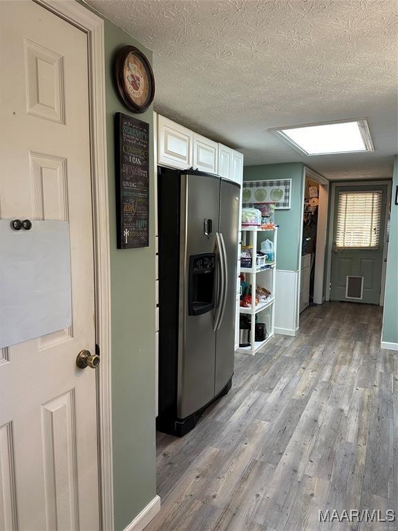 kitchen featuring white cabinets, light wood-type flooring, a textured ceiling, and stainless steel refrigerator with ice dispenser