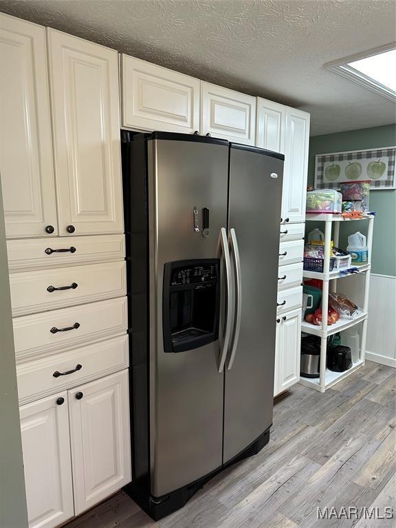 kitchen featuring white cabinets, light wood-style floors, a textured ceiling, and stainless steel fridge