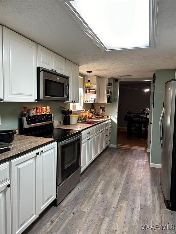 kitchen with a sink, appliances with stainless steel finishes, wood finished floors, and white cabinetry
