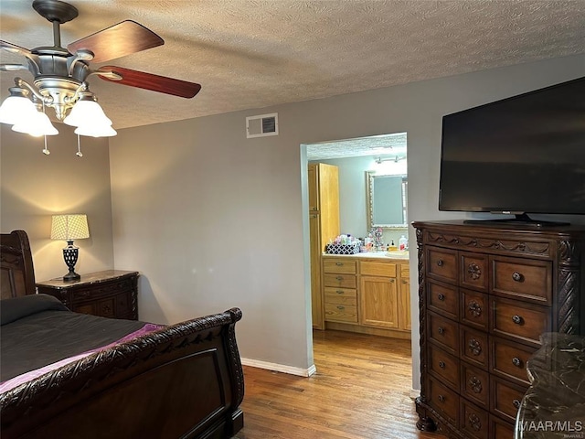 bedroom featuring visible vents, baseboards, ensuite bathroom, a textured ceiling, and wood finished floors