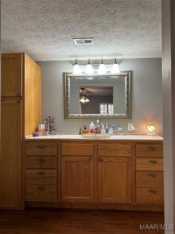 bathroom with vanity, visible vents, a textured ceiling, and wood finished floors