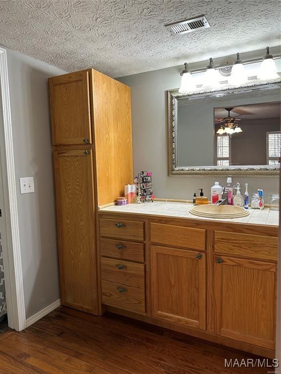 bathroom with vanity, visible vents, a textured ceiling, and wood finished floors