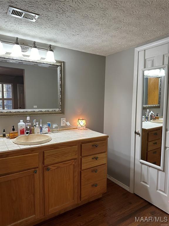 bathroom with a textured ceiling, vanity, visible vents, wood finished floors, and baseboards