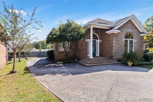 view of front of property featuring driveway, brick siding, a front yard, and fence