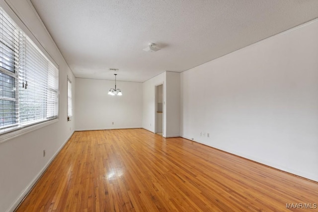 spare room with a textured ceiling, light wood finished floors, baseboards, and an inviting chandelier