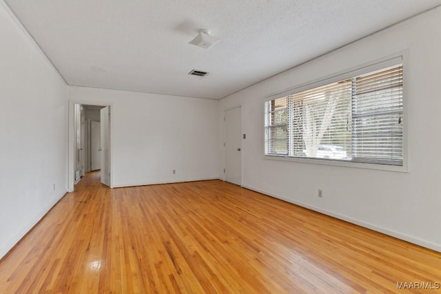 spare room featuring light wood-type flooring, baseboards, visible vents, and a textured ceiling