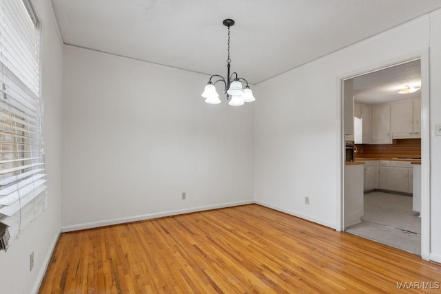 spare room with light wood-type flooring, an inviting chandelier, and baseboards