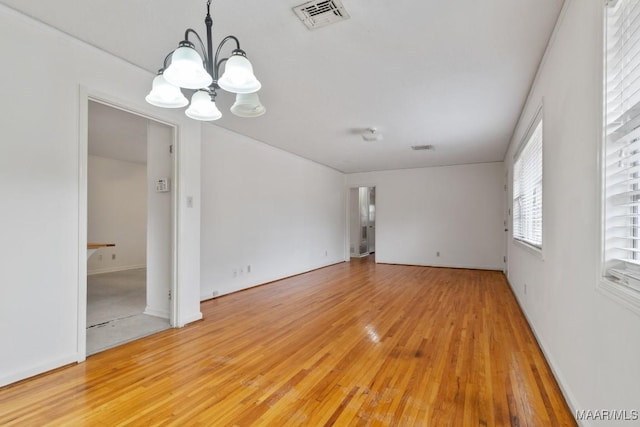 unfurnished room featuring light wood-type flooring, visible vents, and a notable chandelier