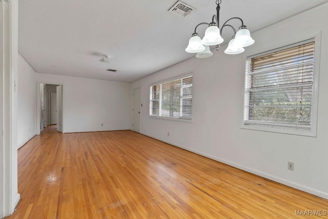 empty room featuring a textured ceiling, visible vents, baseboards, light wood-style floors, and an inviting chandelier