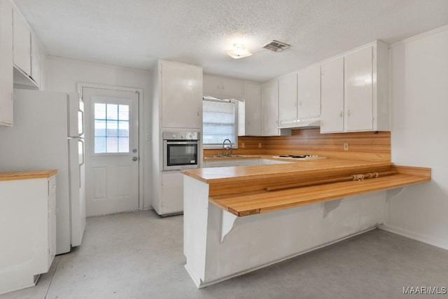 kitchen with under cabinet range hood, a peninsula, white appliances, a sink, and visible vents