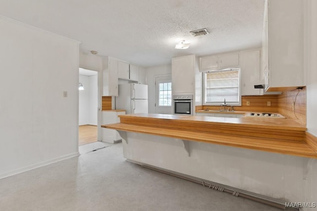 kitchen featuring a textured ceiling, a peninsula, white appliances, concrete floors, and visible vents