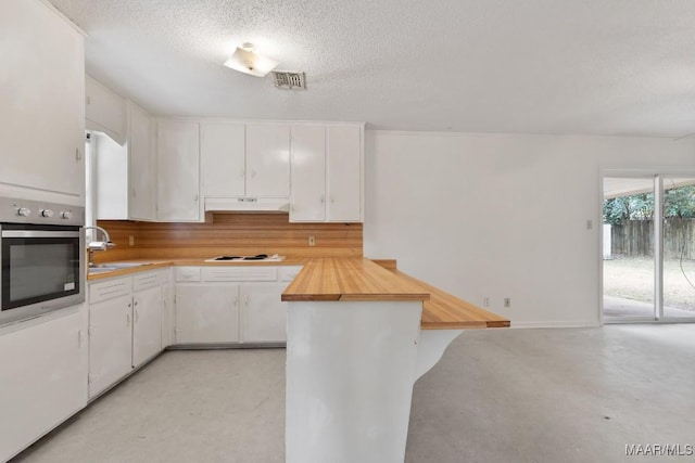 kitchen with visible vents, wooden counters, stainless steel oven, a sink, and under cabinet range hood