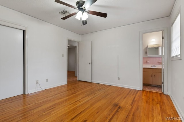 unfurnished bedroom with a closet, visible vents, light wood-style floors, connected bathroom, and a sink