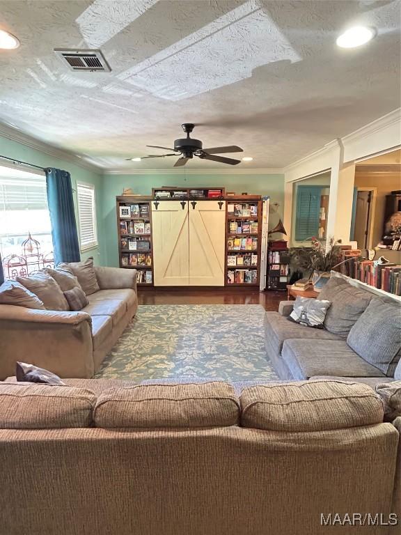 living area with crown molding, visible vents, a ceiling fan, a textured ceiling, and wood finished floors