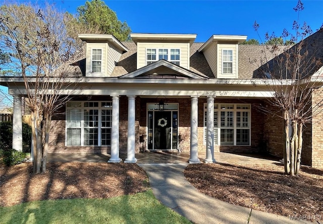 view of front facade featuring a shingled roof, covered porch, and brick siding