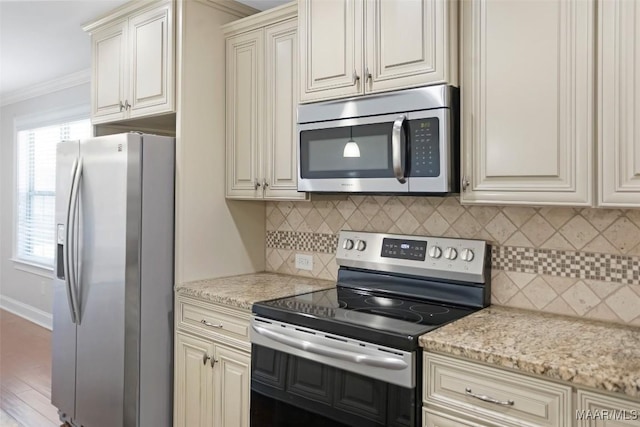 kitchen featuring appliances with stainless steel finishes, cream cabinetry, decorative backsplash, light stone countertops, and crown molding