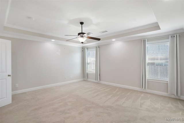 empty room with crown molding, a tray ceiling, visible vents, and light colored carpet