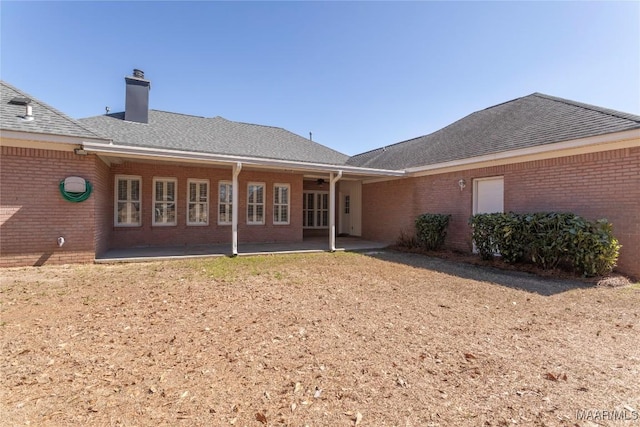 rear view of house featuring brick siding, a chimney, a patio area, and a shingled roof