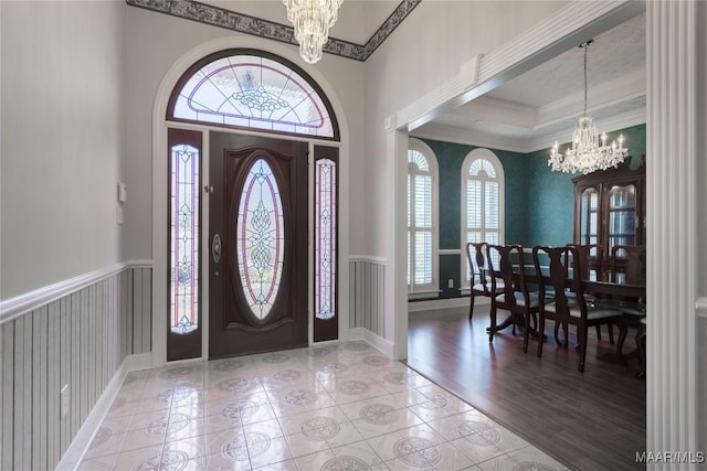 entrance foyer with ornamental molding, light wood-type flooring, a wainscoted wall, and a notable chandelier