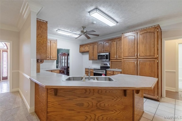 kitchen featuring appliances with stainless steel finishes, brown cabinets, a peninsula, crown molding, and a sink